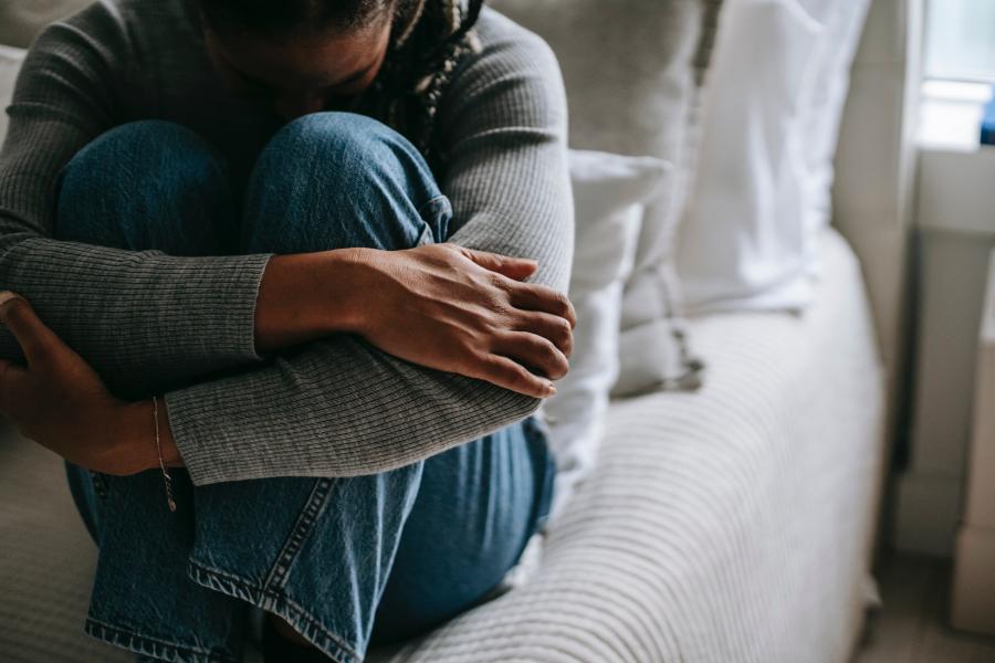 Woman sitting on bed with knees held to chest