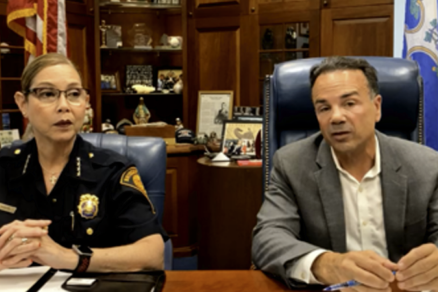 Two people sitting at a desk; one woman who in police uniform, and one man in a suit