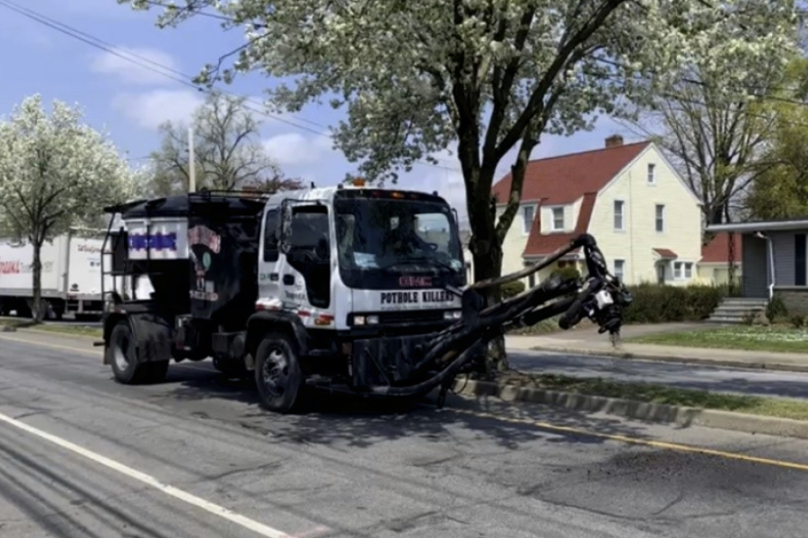 A "pothole killer" work truck clears a pothole on the side of a suburban road