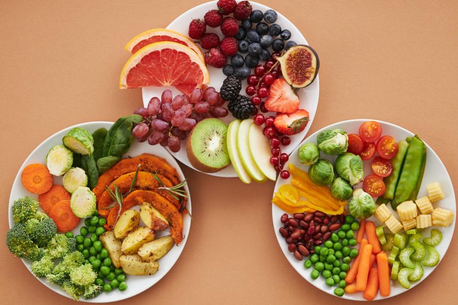 Three white plates on a beige surface filled with a variety of cut fresh fruits and vegetables