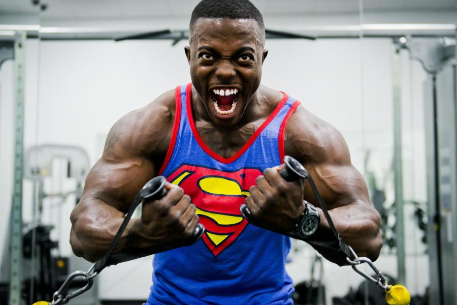 Man with muscles wearing superman tank top yelling intensely while exercising