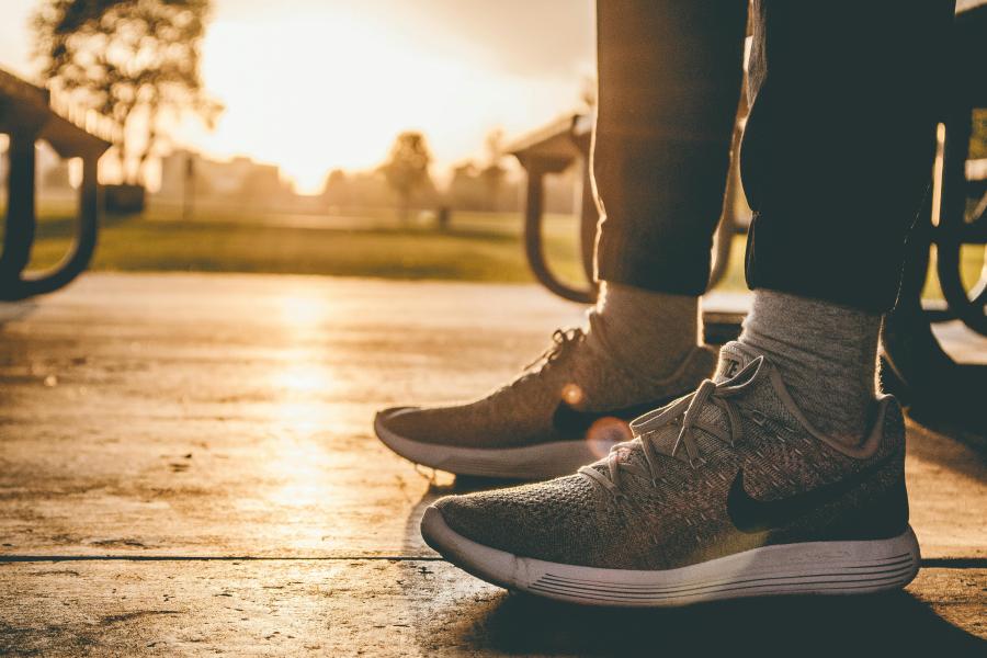 A close up picture of grey running shoes of someone standing on pavement with a sunset in the background.