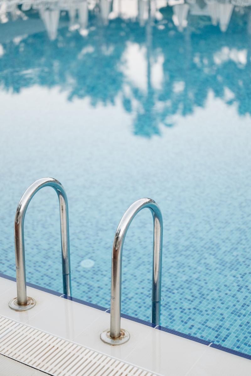 Swimming pool ladder with palm trees reflected on the water