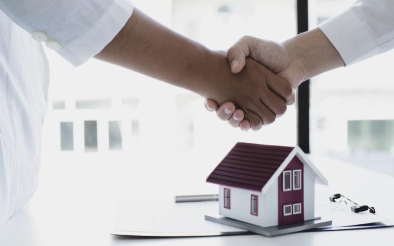 Two people shaking hands with a wooden house in the background