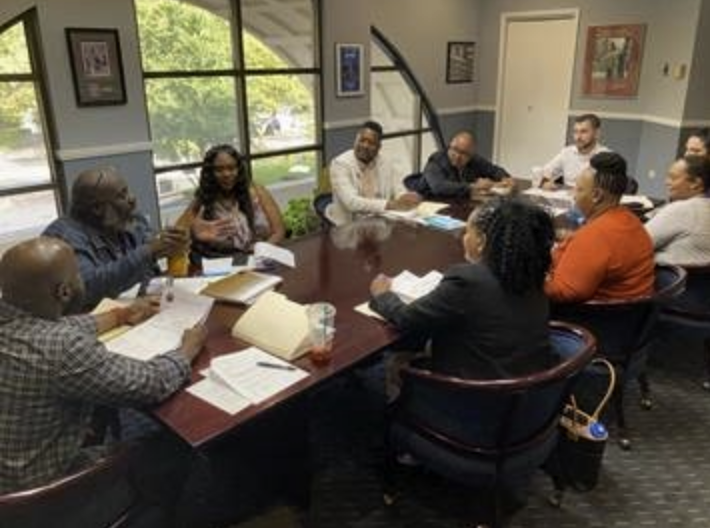 8 people sit around a large table in an office