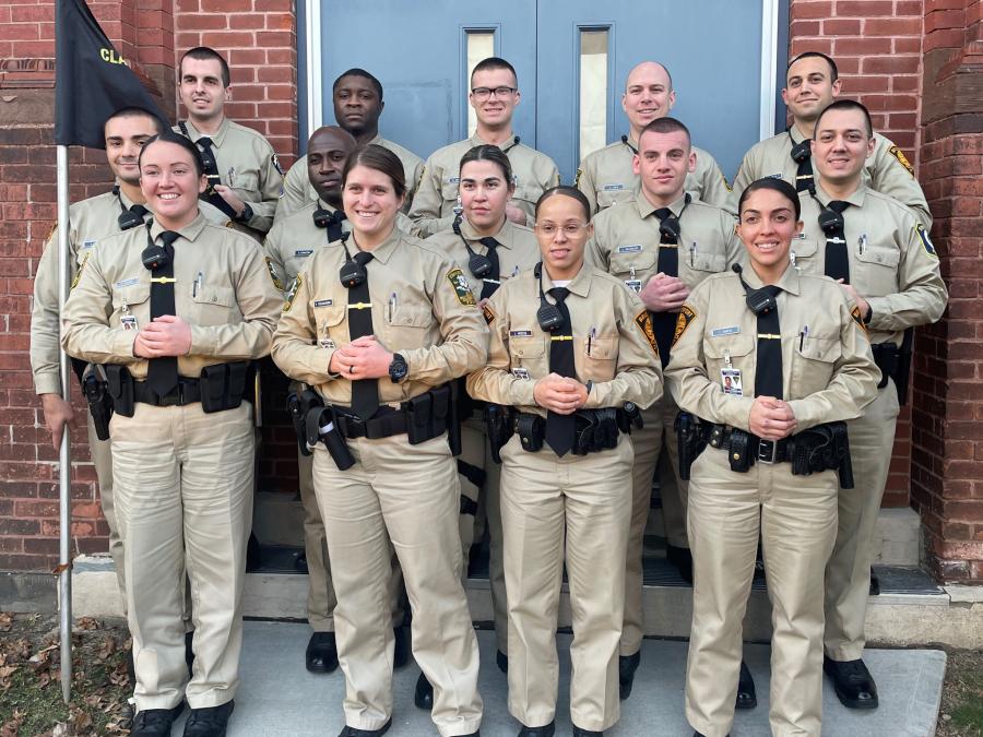 Photo of class 44 police recruits in uniform, standing in front of the front door of the Bridgeport Police Academy.