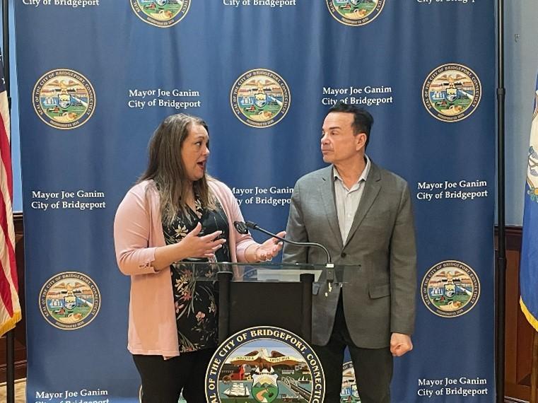 Mayor Ganim and Dr. Rivera-Rodriguez standing at the City of Bridgeport podium in the Mayor's Back Conference Room, discussing the grant awarded by the U.S. Conference of Mayors