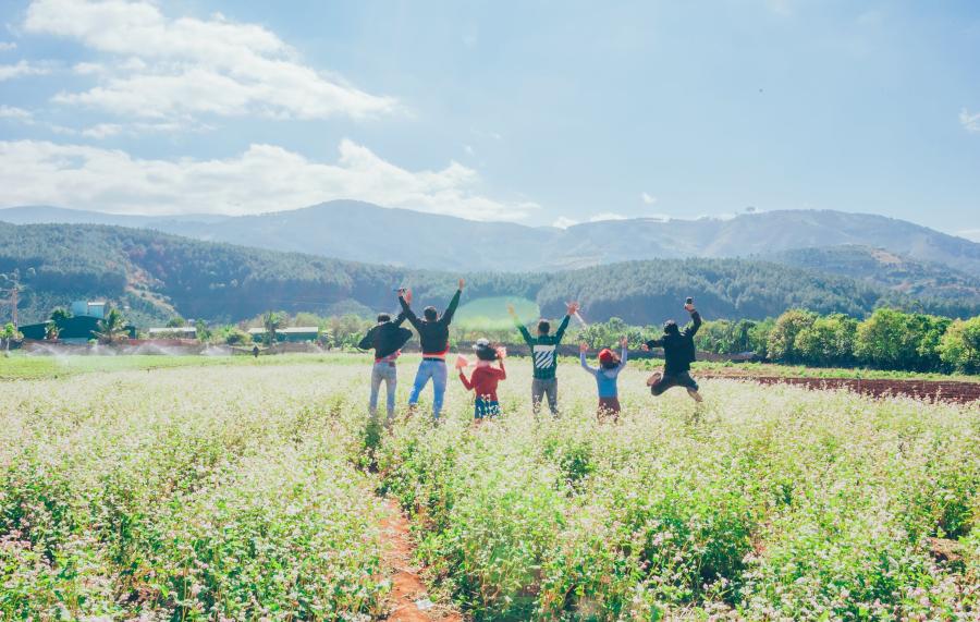 Six kids jumping in a sunny field with mountains in the background