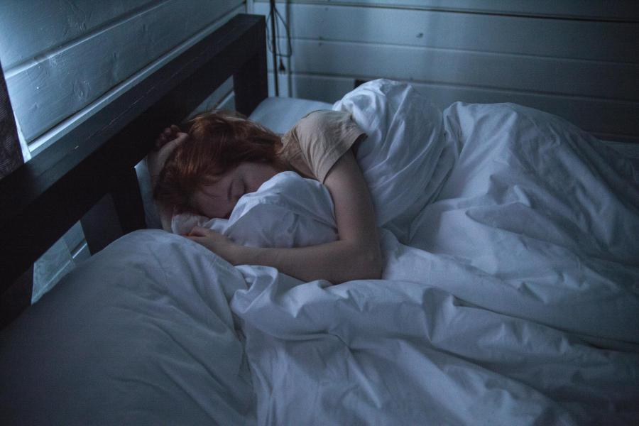 A woman sleeping in a bed in a dark room with her face covered by blankets